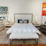 shaggy white bench in front of a bed with a square bedframe and a white quilted bedspread