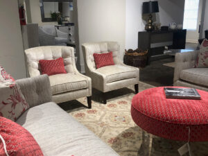 Two armless Stanford chairs in taupe near a taupe-colored couch and footstool decorated with red pillows