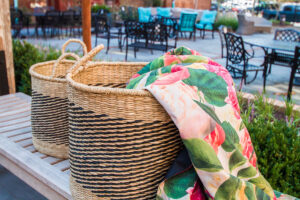 floral fabric spilling out of a woven basket in front of outdoor wrought iron patio furniture